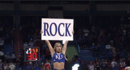 A Cheerleader Holds Up A Sign That Reads Rock GIF