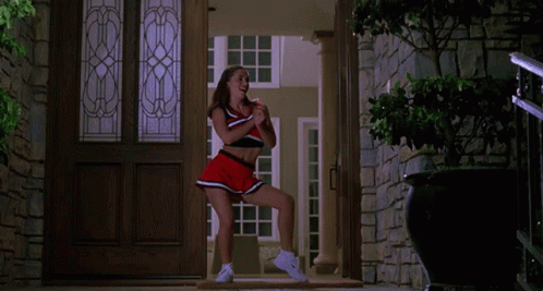 A Cheerleader In A Red And Black Outfit Is Dancing In A Doorway GIF