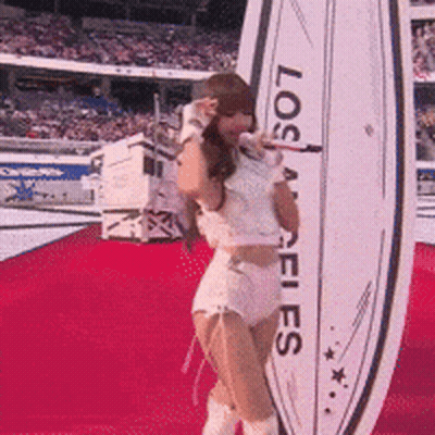 A Cheerleader Is Singing Into A Microphone In Front Of A Los Angeles Sign GIF