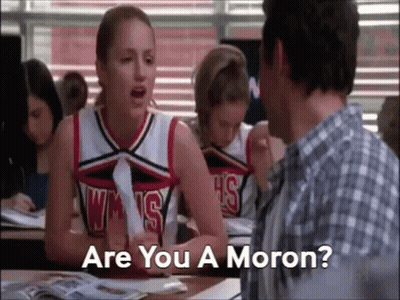 A Cheerleader Is Sitting At A Desk Talking To A Man In A Classroom While A Man Looks On . GIF