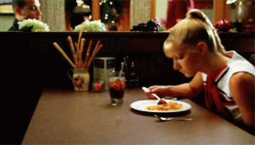 A Cheerleader Sits At A Table With A Plate Of Food On It GIF
