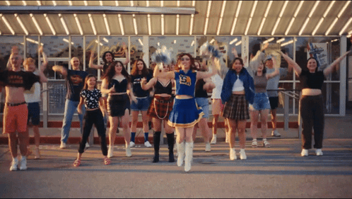 A Cheerleader With The Number 15 On Her Top Is Surrounded By Other Cheerleaders GIF