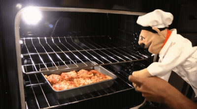 A Chef Puppet Is Looking At A Pan Of Food In The Oven GIF