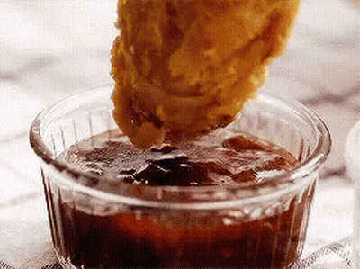 A Chicken Nugget Is Being Dipped Into A Small Bowl Of Sauce . GIF