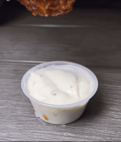 A Chicken Wing Is Being Dipped Into A Small Cup Of Ranch Dressing GIF