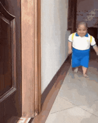 A Child In Blue Shorts And A White Shirt Is Walking Down A Hallway GIF