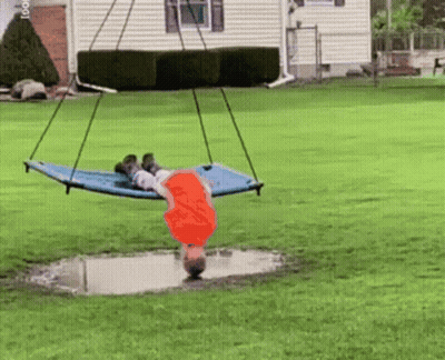 A Child Is Laying On A Blue Hammock In A Yard GIF