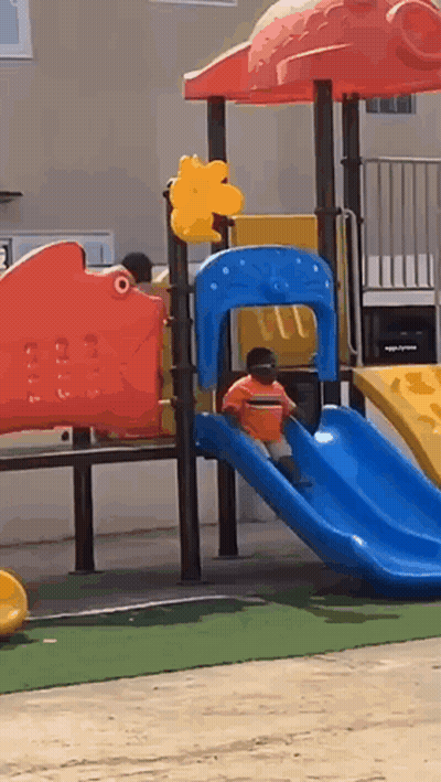 A Child Is Playing On A Slide At A Playground . GIF