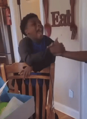 A Child Sitting In A Chair With A Sign That Says Eat On The Wall Behind Him GIF