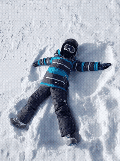 A Child Wearing A Helmet And Goggles Lays In The Snow GIF