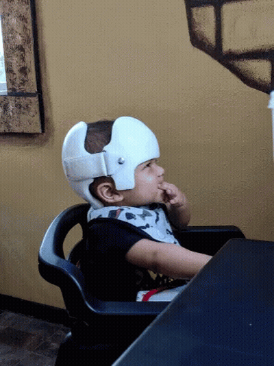 A Child Wearing A White Helmet Is Sitting In A Chair GIF