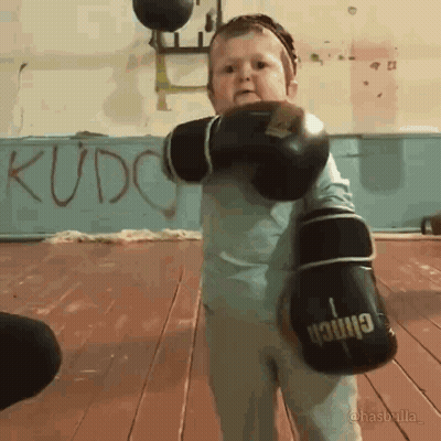 A Child Wearing Boxing Gloves With The Word Kudo On The Wall Behind Him GIF