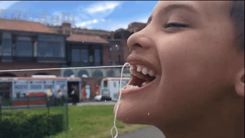 A Child With A String In His Mouth And A Building In The Background GIF