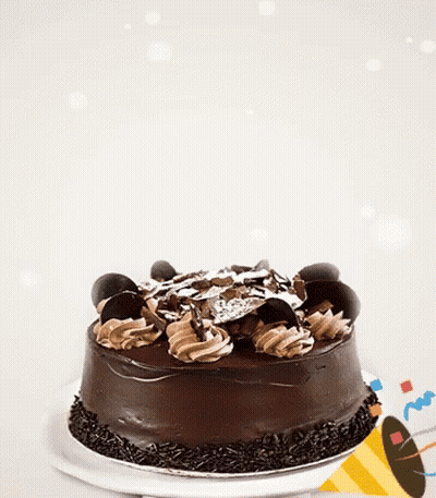 A Chocolate Cake Is On A White Plate With A Party Hat In The Background GIF