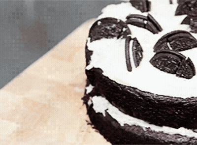 A Chocolate Cake With Oreos On Top Is On A Wooden Table GIF