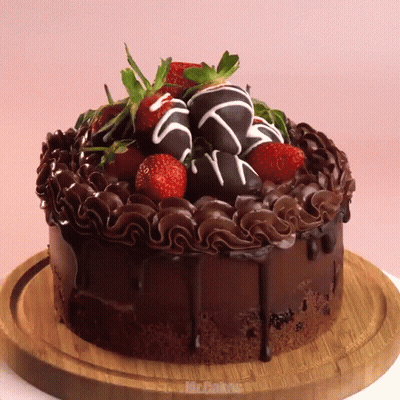 A Chocolate Cake With Strawberries On Top Is On A Cutting Board GIF
