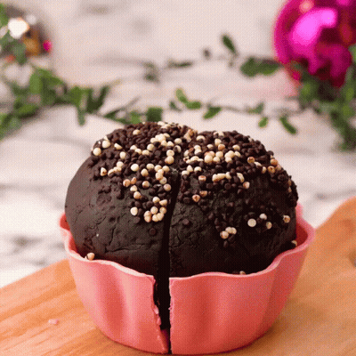 A Chocolate Cupcake In A Pink Cup With Sprinkles On It GIF