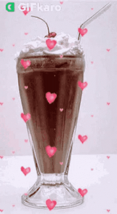 A Chocolate Milkshake With Whipped Cream And A Cherry On Top Is Surrounded By Pink Hearts . GIF
