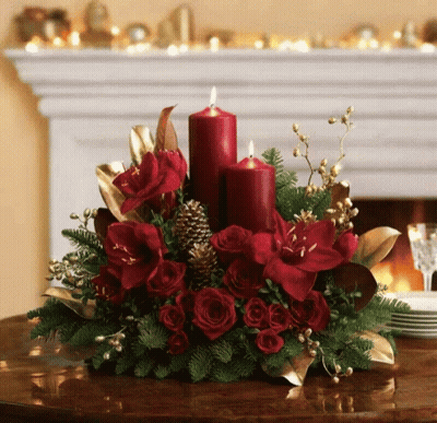A Christmas Centerpiece With Red Candles And Red Flowers GIF