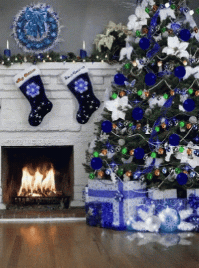 A Christmas Tree With Blue And Green Decorations And A Fireplace With Two Stockings Hanging From It GIF