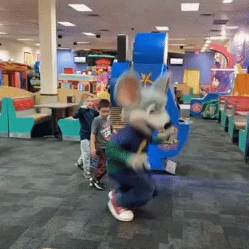A Chuck E Cheese Mascot Is Dancing With Two Young Boys In A Restaurant GIF