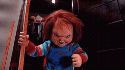A Chucky Doll Is Standing In A Doorway Holding A Stick . GIF