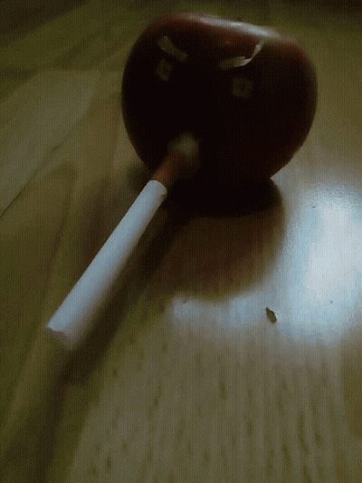 A Cigarette Is Sitting On A Table Next To An Apple That Has The Letter B On It GIF