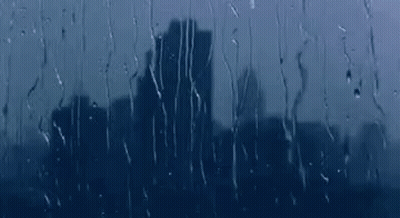 A City Skyline Is Reflected In A Window With Rain Drops On It . GIF