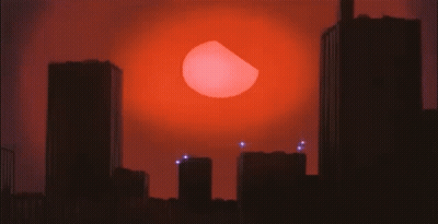 A City Skyline With A Large Red Sun Behind It GIF