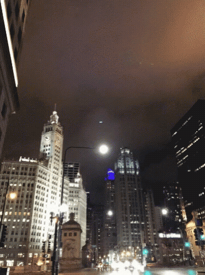 A City Street At Night With A Clock Tower And A Building That Says ' Bank Of America ' On It GIF