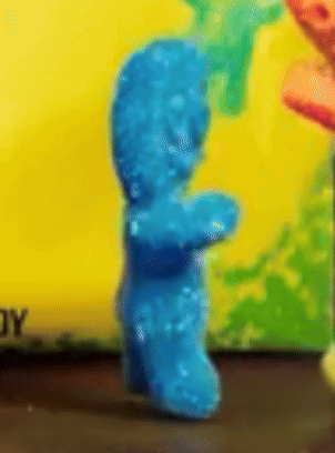 A Close Up Of A Blue Gummy Bear With A Yellow Background GIF