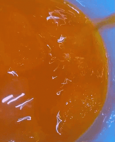 A Close Up Of A Bowl Of Orange Liquid With A Yellow Spoon In It GIF