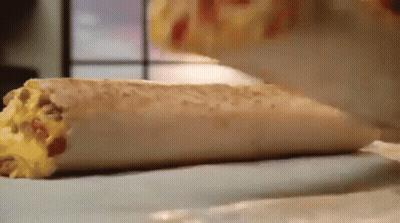 A Close Up Of A Burrito On A Table Being Eaten . GIF