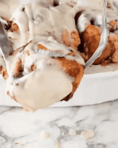 A Close Up Of A Cinnamon Roll With Icing And A Spoon In It . GIF