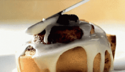 A Close Up Of A Cinnamon Roll With White Frosting On It GIF