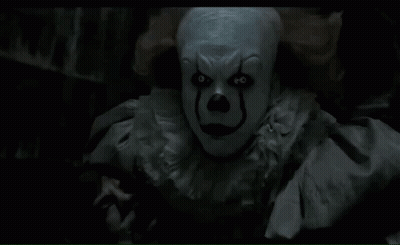 A Close Up Of A Clown In A Dark Room Looking At The Camera GIF