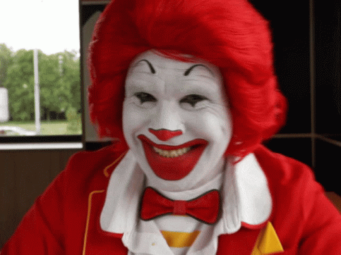 A Close Up Of A Clown With Red Hair And White Face Paint GIF