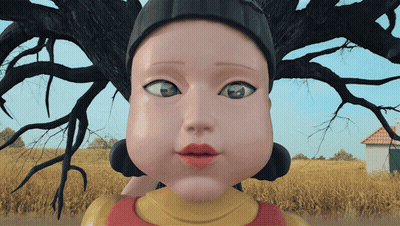 A Close Up Of A Doll 'S Face With A House In The Background GIF