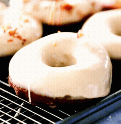 A Close Up Of A Donut With White Frosting On A Cooling Rack GIF