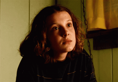 A Close Up Of A Girl 'S Face With A Yellow Curtain Behind Her GIF