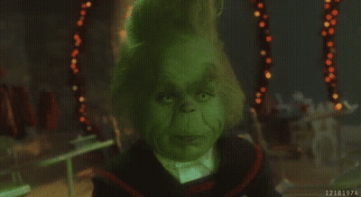 A Close Up Of A Grinch 'S Face In A Dark Room With Christmas Lights In The Background . GIF
