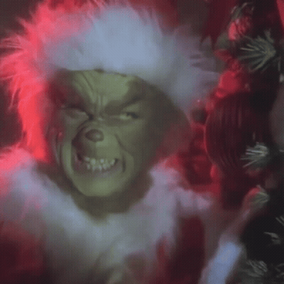 a close up of a grinch 's face with a wreath in the background .