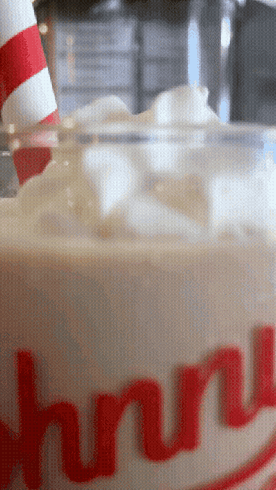 A Close Up Of A Johnny 'S Milkshake With Whipped Cream And A Red And White Striped Straw GIF