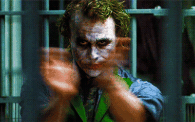 A Close Up Of A Joker Behind Bars With His Hands Outstretched GIF