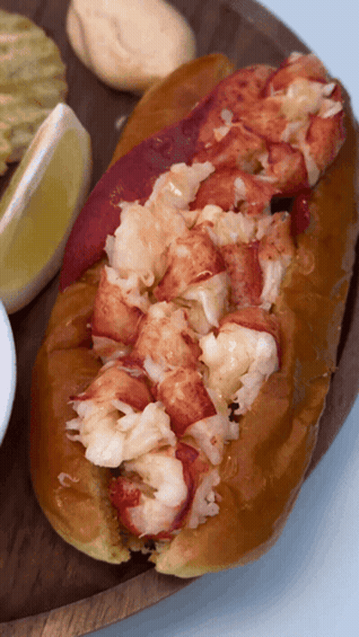 A Close Up Of A Lobster Roll On A Wooden Tray GIF