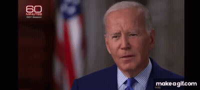 A Close Up Of A Man In A Suit And Tie With An American Flag In The Background . GIF