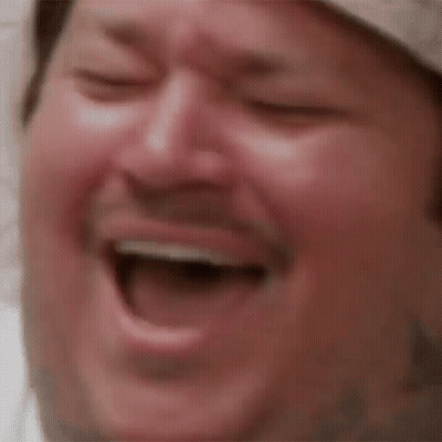 A Close Up Of A Man Laughing With His Eyes Closed And His Mouth Open . GIF