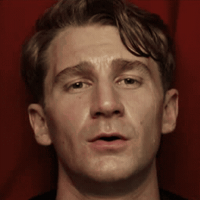 A Close Up Of A Man 'S Face Against A Red Curtain GIF