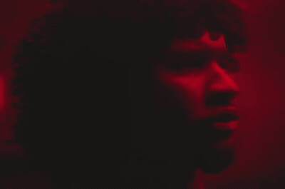 A Close Up Of A Man 'S Face In A Dark Room With A Red Light Behind Him GIF