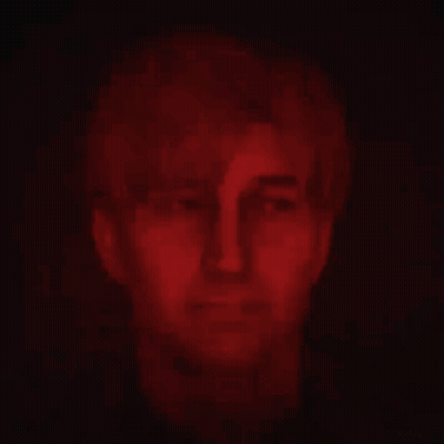 A Close Up Of A Man 'S Face In A Dark Room With Red Lights Behind Him . GIF